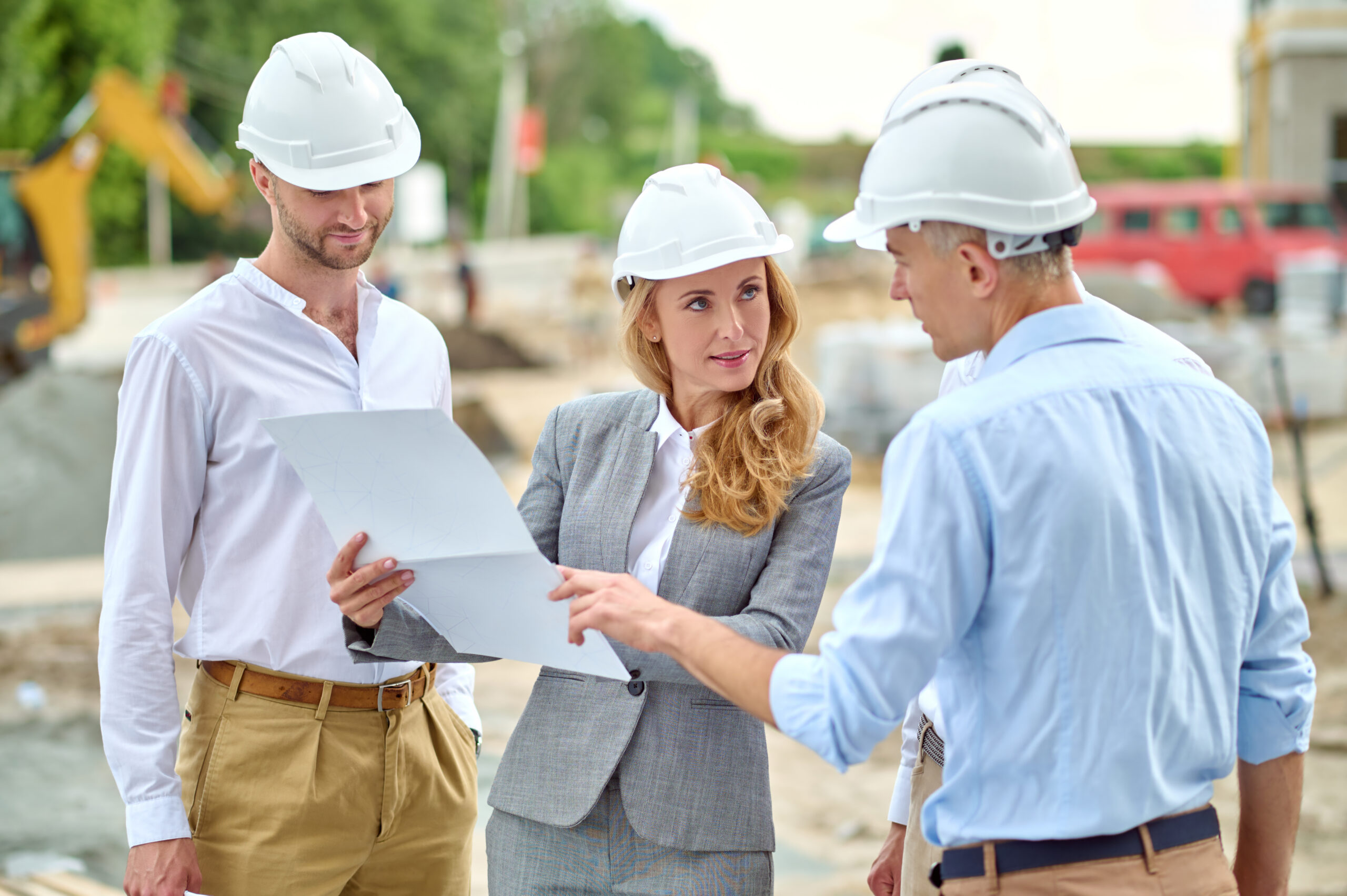 Responsibility. Determined blonde woman in safety helmet showing document looking questioningly at work group leader man at construction site